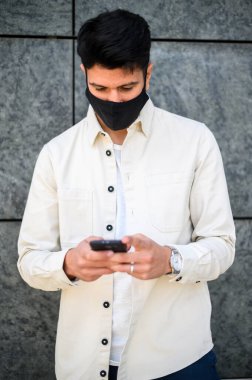 Koronavirüs covid-19 salgınına karşı koruyucu maske takan adam akıllı telefonunu kullanıyor.