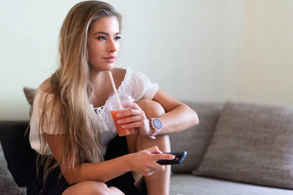 テレビを見ながら自宅でグレープフルーツジュースを飲むためにわらを使用して女性 — ストック写真