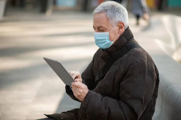 Covidコロナウイルスのライフスタイル マスクされた高齢者ビジネスマン彼のタブレットを使用して市の広場に屋外に座っている間 — ストック写真