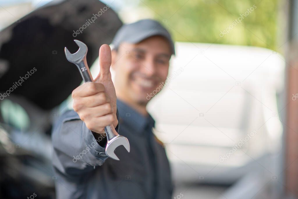 Car mechanic giving thumbs up with a wrench in hand