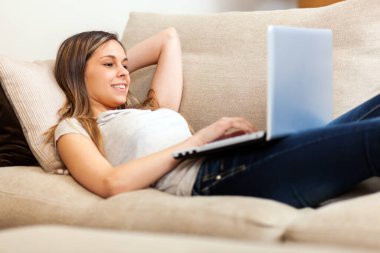 Kanepede dinlenirken dizüstü bilgisayar kullanan bir kadın.