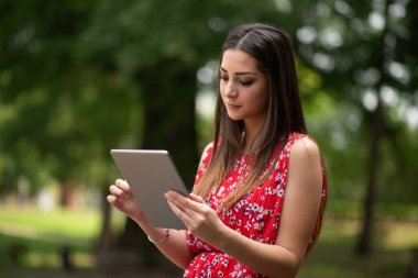 Parkta dijital tablet kullanan genç bir kadın.