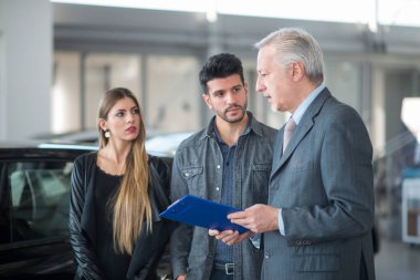 Genç bir aile satıcıyla konuşuyor ve yeni arabalarını galeride seçiyorlar.