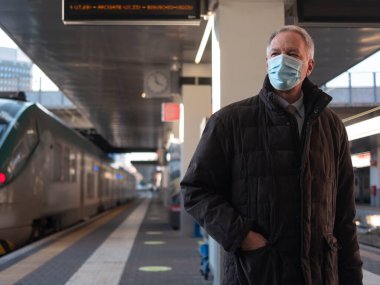 Coronavirus covid seyahat konsepti, kıdemli iş adamı istasyonda bir trenin yanında yürüyor.