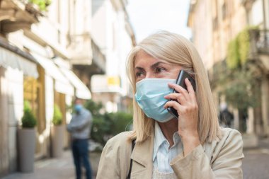Maske takmış bir kadın telefon görüşmesi yapıyor. Koronavirüs salgını.