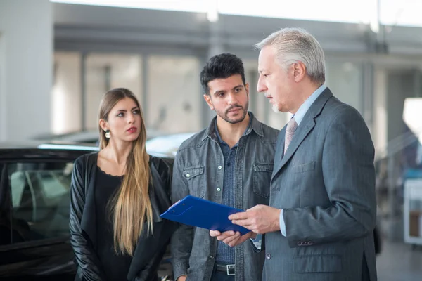 Jovem Família Conversando Com Vendedor Escolhendo Seu Novo Carro Showroom — Fotografia de Stock