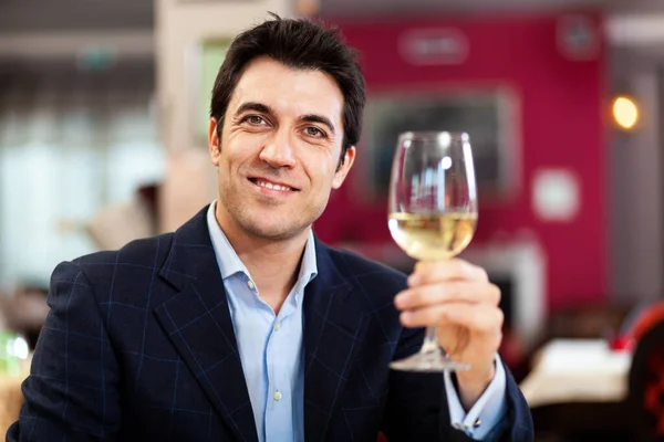 一个英俊的男人在餐馆里端着一杯白葡萄酒 — 图库照片