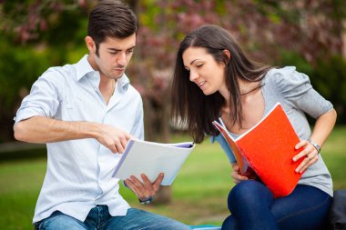 İki öğrenci açık hava bankında birlikte ders çalışıyor.