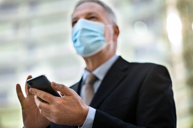Üst düzey yönetici Coronavirus salgınından korunmak için maske takarken akıllı telefonunu açık havada kullanır.