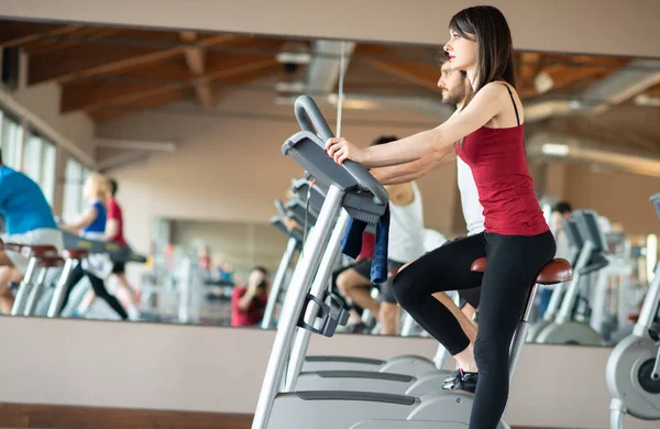 适合的女人骑着固定自行车在健身房里锻炼 — 图库照片