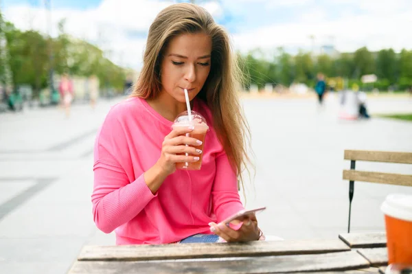 快乐的年轻女人一边在户外喝咖啡一边用智能手机 — 图库照片