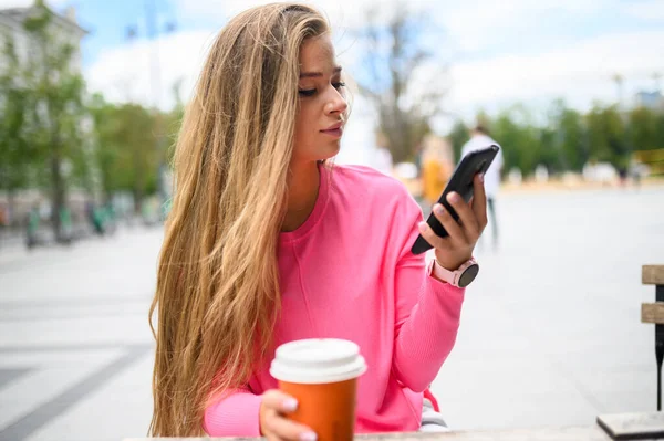 快乐的年轻女人一边在户外喝咖啡一边用智能手机 — 图库照片