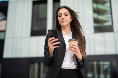 Modern şehir meydanında akıllı telefonunu kullanan bir iş kadını.