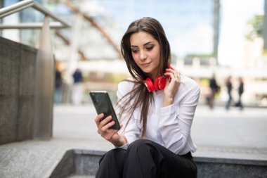 Genç bir kadın merdivenlerde otururken cep telefonunu kullanıyor.