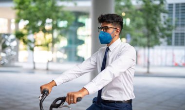 Maskeli işadamı bisikletini ofisin önüne park ediyor.