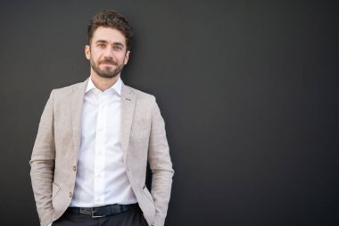 Siyah bir duvarın yanında duran yakışıklı bir iş adamı.