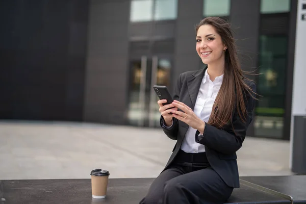 Ofisinin Yanındaki Bankta Otururken Akıllı Telefonunu Kullanan Gülümseyen Bir Kadını — Stok fotoğraf