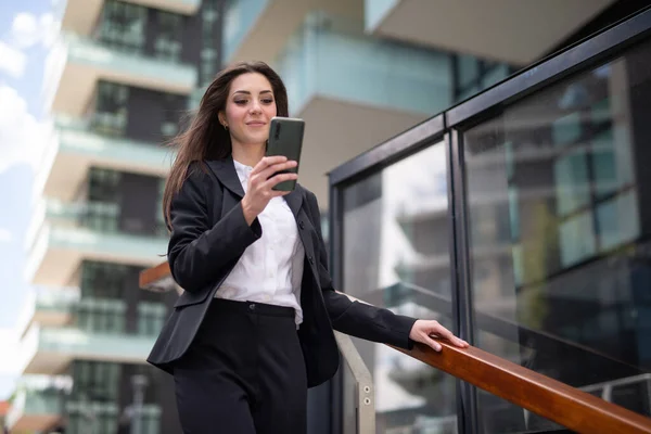 在一个现代化的城市里 年轻的女商人在下楼梯的时候用她的智能手机 — 图库照片