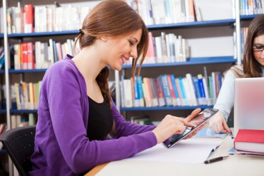 Bir kitaplıkta bir tablet kullanan kadın