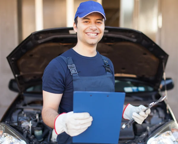 Mechanic holding a clipboard in front of a car — Stock Photo, Image