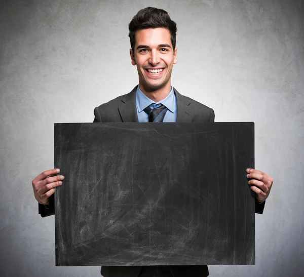 Empresário sorridente segurando um quadro negro — Fotografia de Stock