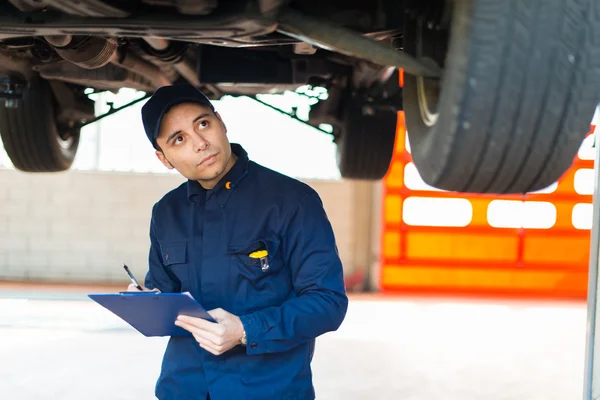 Mechanic schrijven op klembord onder auto — Stockfoto