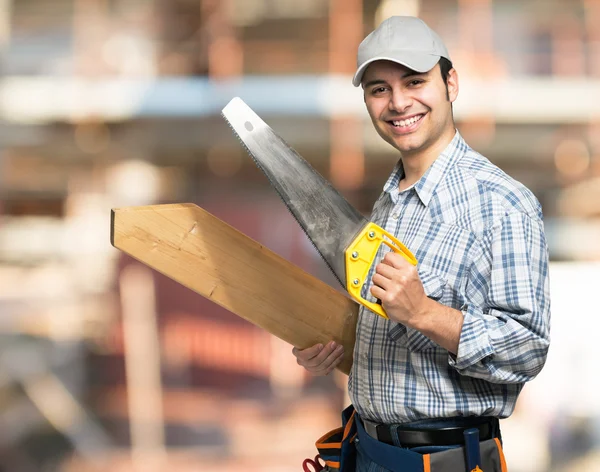 Carpintero sosteniendo tablón de madera y sierra — Foto de Stock