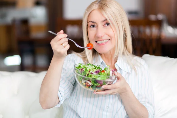 Vrouw die salade eet op de bank — Stockfoto