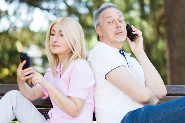 Par använder telefoner på park — Stockfoto