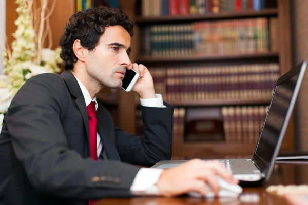 Businessman using laptop talking on phone — Stock Photo, Image