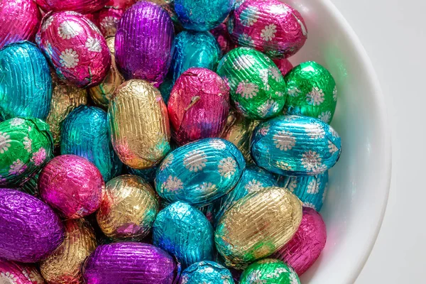 盛满巧克力糖果蛋的白色碗 复活节用彩色铝箔 免版税图库图片