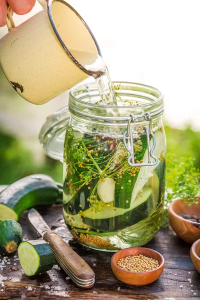 Verser l'eau dans un bocal avec des courgettes et des épices — Photo