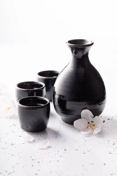 日本酒を伝統的なアルコールとして 伝統的に陶器で酒を出す 白い石の上に黒い陶器 — ストック写真