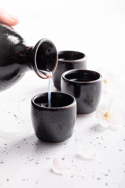 Strong sake as traditional alcohol. Japanese habit of drinking alcohol. Black ceramics on a white stone.