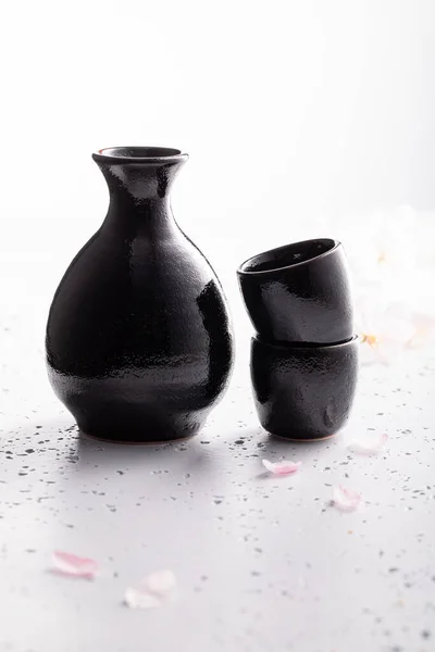 桜の咲く濾過されていない酒 伝統的に陶器で酒を出す 白い石の上に黒い陶器 — ストック写真