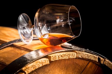 Glass of cognac on the old wooden barrel clipart