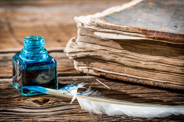 Pluma blanca sobre tintero azul y libro viejo — Foto de Stock