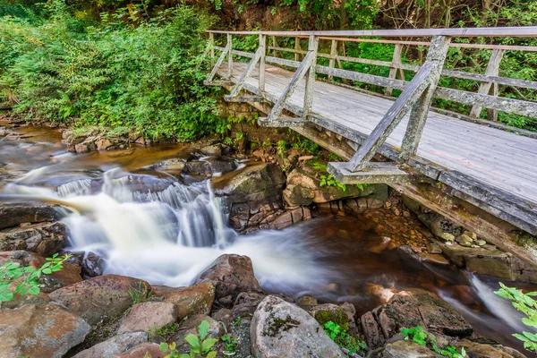 Ruscello di montagna che scorre sotto un ponte di legno — Foto Stock