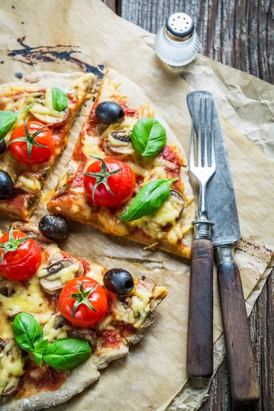 Färsk pizza på papper och gamla träbord — Stockfoto