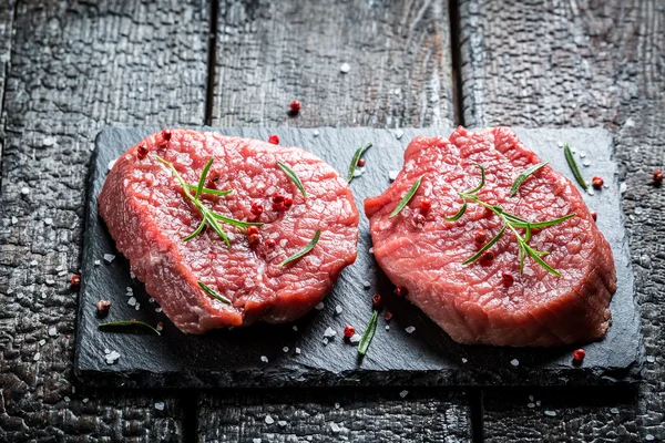 Trozo de carne de res con romero y pimienta sobre roca negra — Foto de Stock
