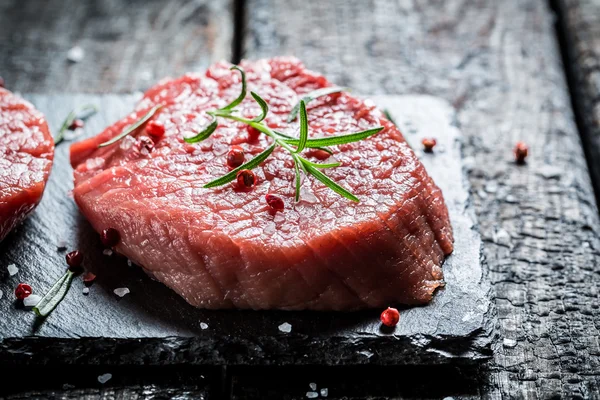 Piece of meat with rosemary and pepper on black rock — Stock Photo, Image