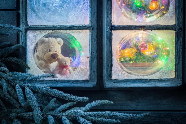 Ведмедик на Різдво в замерзлому вікні з деревом і вогнями — стокове фото