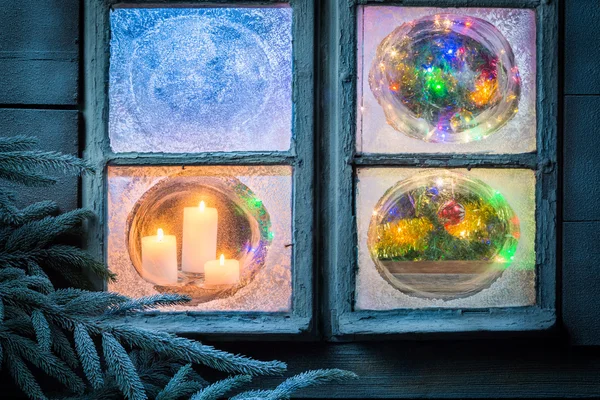 Beautiful burning candles for Christmas in frozen window — Stock Photo, Image
