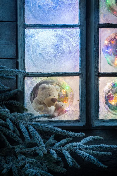 Osito de peluche en ventana congelada para Navidad con árbol y luces — Foto de Stock