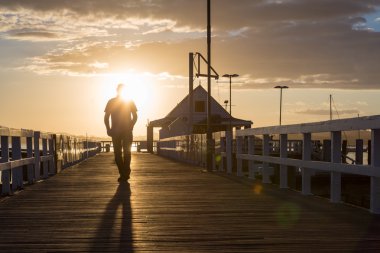 İskelede gün batımında yürüyen bir adam