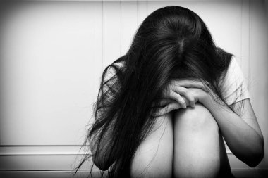 Asyalı kadın yerde tek başına oturmuş dizlerini kucaklıyor, üzgün hissediyor ve büyük depresif bozukluk, kırık kalp ya da uykusuzluk çekiyor. Ruh sağlığı ya da psikolojik konsept. Siyah-beyaz tonu.