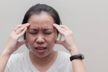 Çıplak omuzlu Asyalı bir kadının portresi şakaklarına dokunuyor. Beyaz arka planda acı ya da stres hissediyor.