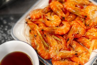 A close-up of a plate piled high with perfectly steamed whole shrimps (prawns) with bright orange shells, served alongside a small bowl of dark dipping sauce. This image illustrates fresh, delicious Chinese or Asian seafood cuisine