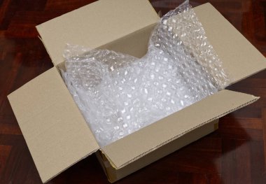 Üzerinde şeffaf plastik baloncuk ambalajı bulunan açık kahverengi bir karton kutunun, koyu ahşap parke zemin üzerine yerleştirilmiş yüksek açılı bir çekimi.