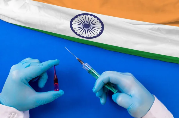 India Vaccination. Hands of doctor holding syringe and coronavirus (COVID-19) vial vaccine on flag India